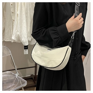 Detail view of white crescent bag with black contrast trim and adjustable wide shoulder strap