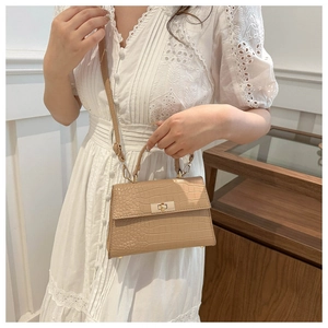 Detail of beige croco-embossed handbag with gold twist lock and adjustable strap