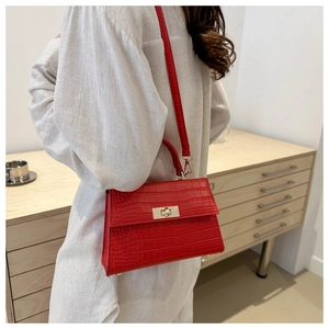 Detailed view of red crocodile-embossed handbag with gold clasp and matching shoulder strap