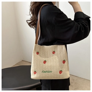Detail of straw tote bag with strawberry embroidery and brown leather shoulder straps