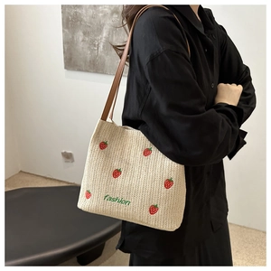 Detail of straw tote bag with strawberry embroidery and brown leather shoulder straps