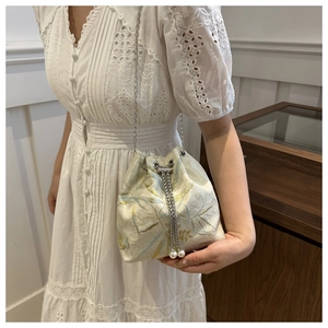 Detail of drawstring bucket bag with leaf pattern, chain strap and pearl accents
