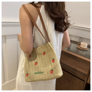 Detail of straw tote bag with strawberry embroidery and leather shoulder straps