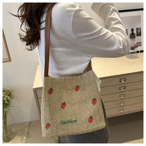 Detail of straw shoulder bag featuring red strawberry embroidery and brown leather strap