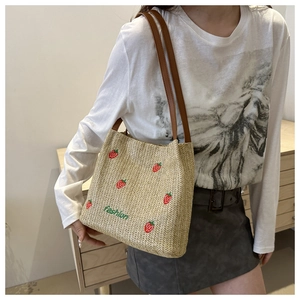 Detailed view of beige straw tote bag with red strawberry embroidery and brown leather straps