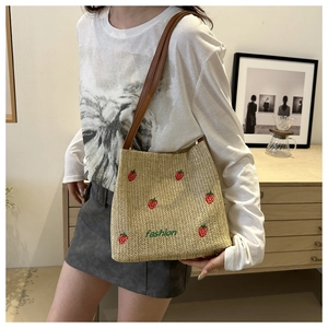 Detail of straw shoulder bag with strawberry embroidery and leather strap in soft indoor light