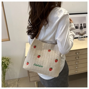 Detail of straw shoulder bag featuring red strawberry embroidery and brown leather strap