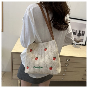 Detail of strawberry embroidery on beige woven straw shoulder bag with fashion text