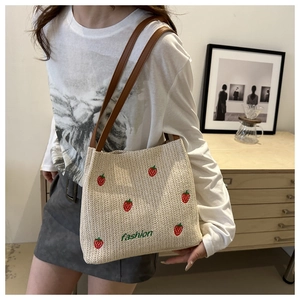 Close-up of strawberry embroidery and woven texture on a beige straw tote bag