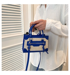 Détail du sac à bandoulière en cuir bleu et paille tressée tenu par un mannequin chic