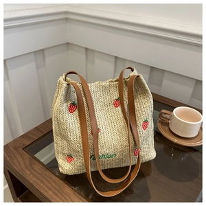 Detail of straw tote bag featuring red strawberry embroidery and brown faux leather straps