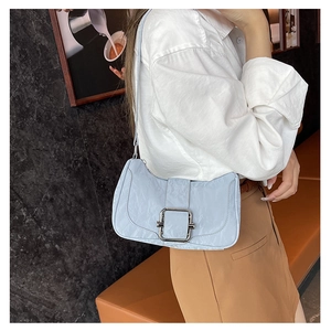 Close-up of light blue underarm bag with silver square buckle on a model in a cafe