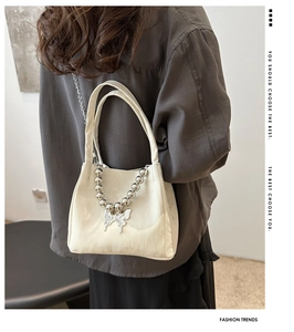 Chic cream-colored bucket bag with silver chain and butterfly charm worn by a model