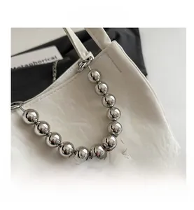 Detail of white pleated handbag featuring oversized silver bead chain and metal charms