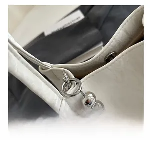 Detail of white lychee grain leather bucket bag featuring silver beaded chain strap and rings