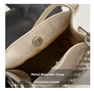 Detail view of cream bucket bag showing magnetic snap closure and silver ball chain