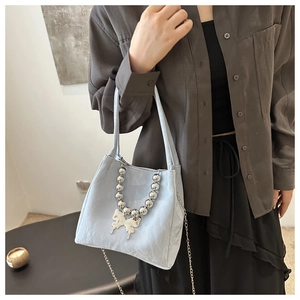Detail of light blue textured bucket bag featuring silver beaded handle and butterfly charm