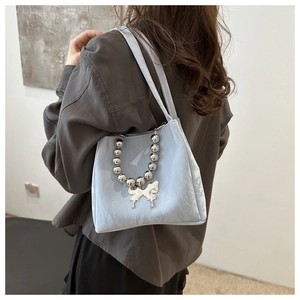 Detail of light blue textured handbag with silver beaded chain and butterfly charm