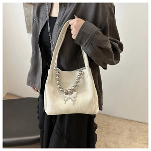 Detail of creamy white PU bucket bag featuring silver ball chain and butterfly pendant