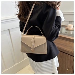 Sac bandoulière en cuir beige avec boucle dorée porté par un mannequin en extérieur