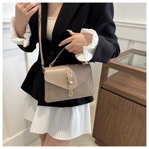 Sac carré beige chic avec boucle en fer à cheval dorée porté sur un blazer noir