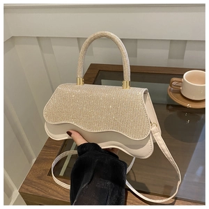 Elegant sequined beige handbag with wavy flap and round top handle in a cafe setting