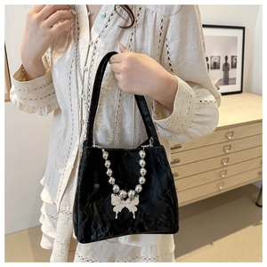 Detail of black textured bucket bag with silver bead chain and butterfly pendant