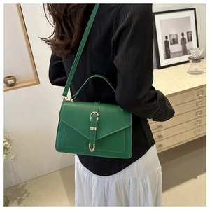 Sac bandoulière vintage en cuir vert avec boucle dorée présenté dans un décor d'intérieur