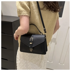 Détail d'un sac à bandoulière noir avec boucle dorée et poignée supérieure en cuir chic