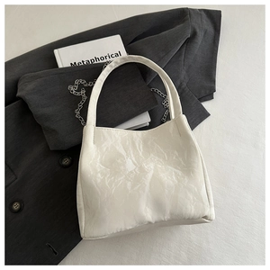 Detail of the pleated texture and silver chain strap on a cream white bucket bag