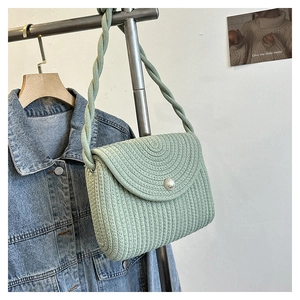 Detail of light green woven straw bag featuring a central pearl and rope shoulder strap