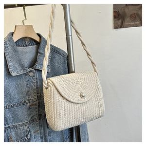 Detail of straw woven crossbody bag with pearl buckle and rope strap on denim jacket