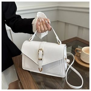 Sac à main blanc en cuir avec boucle dorée posé sur une table basse en bois chic