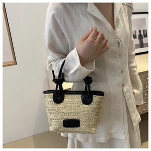 Detailed close-up of woven straw handbag featuring black leather knot handles and trim
