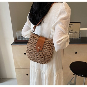 Dettaglio della borsa in paglia intrecciata con patta in pelle marrone su modella
