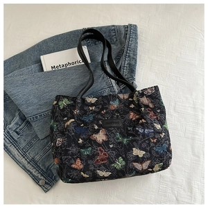 Close-up of woven floral tote bag featuring colorful butterfly patterns and leather handles