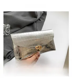 Détail de la pochette enveloppe argentée à motif crocodile avec boucle dorée