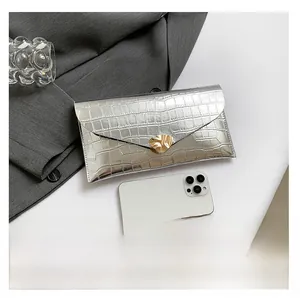 Détail de pochette enveloppe argentée motif crocodile avec fermoir feuille et smartphone