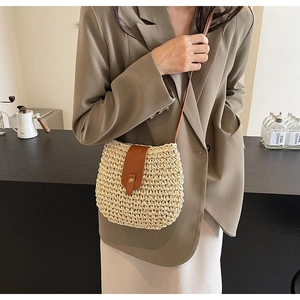 Dettaglio della borsa a tracolla in paglia intrecciata con patta in pelle marrone e fibbia oro
