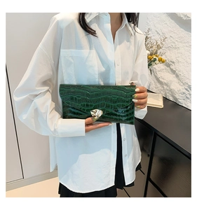 Détail d'une pochette vert foncé en cuir gaufré crocodile avec fermoir métallique chic