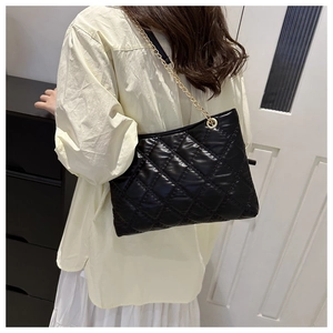 Detail of black quilted shoulder bag with gold chain strap worn by a model in a cozy room