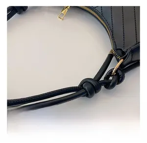 Detail of black leather underarm bag with knotted shoulder strap and gold zipper
