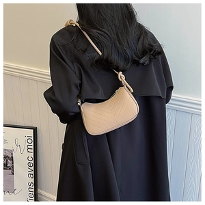 Minimalist beige baguette shoulder bag with V-shaped quilting on model in black coat