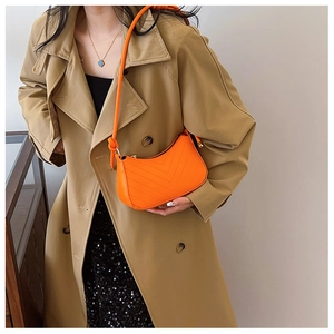 Detail of bright orange crescent underarm bag with V-quilted texture and knot accents