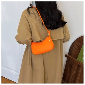 Detail of bright orange hobo bag with V-shaped quilting shown on person with trench coat