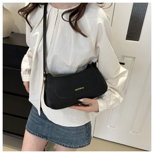 Close-up of minimalist black leather shoulder bag with gold lettering on a model