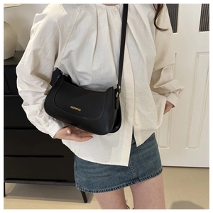 Close-up of a minimalist black faux leather shoulder bag with golden brand lettering