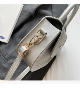 Close-up of premium gold-tone hardware and stitching on a light gray saddle bag