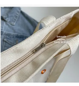 Detail of smooth metal zipper closure on durable cream canvas tote bag with orange embroidery