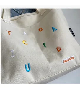 Detail of off-white canvas tote bag featuring colorful letter embroidery and fashion label